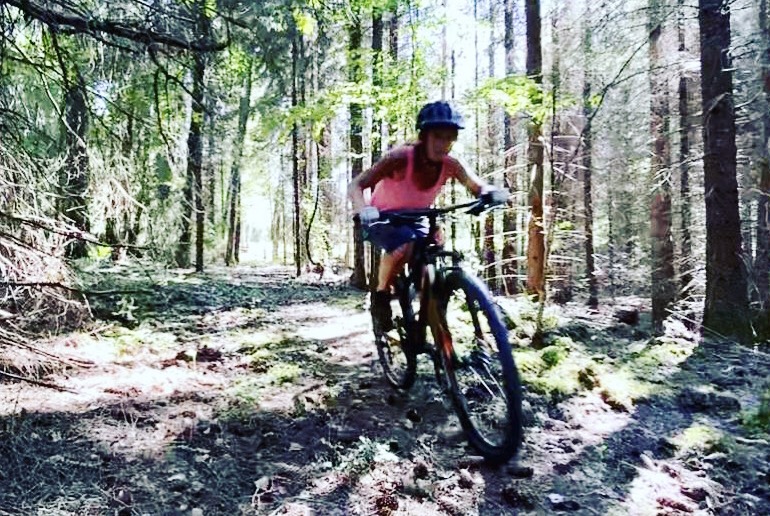 Kvinna cyklar mountainbike i skog.